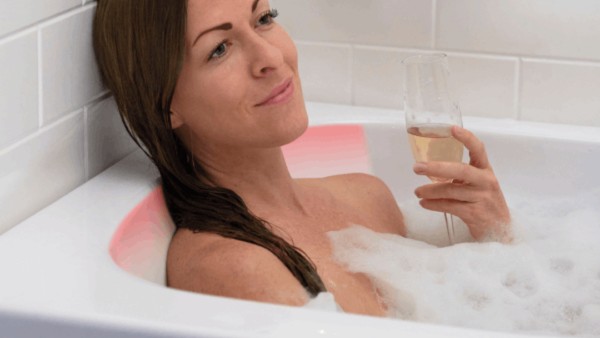 Woman enjoying a warm soak with a heated backrest and a glass of champagne in a walk-in tub