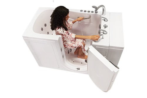 Woman comfortably seated in a walk-in tub with an open outward swinging door, adjusting water settings